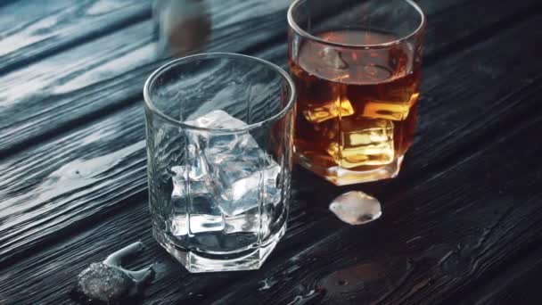 El whisky se vierte en un vaso con hielo sobre una mesa de madera negra. Video de stock