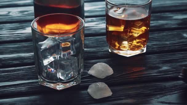 Whiskey wordt gegoten in een glas met ijs op een zwarte houten tafel. — Stockvideo