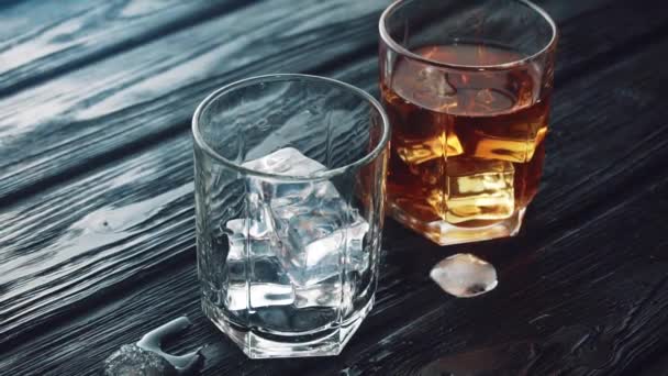 El whisky se vierte en un vaso con hielo sobre una mesa de madera negra. — Vídeos de Stock