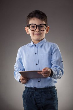 Gri arka planda elektronik tableti olan sevimli bir çocuk.