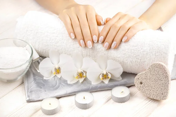 Bela manicure francesa com orquídea, vela e toalha na mesa de madeira branca . — Fotografia de Stock