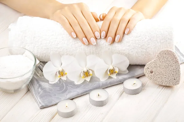 Hermosa manicura francesa con orquídea, vela y toalla en la mesa de madera blanca . — Foto de Stock