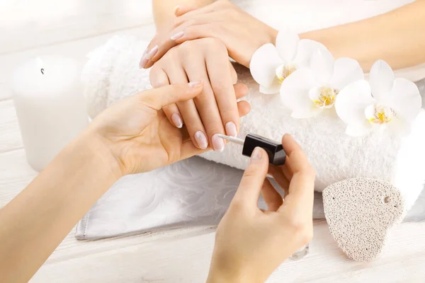 Bella manicure francese con orchidea, candela e asciugamano sul tavolo di legno bianco. mani manicure — Foto Stock