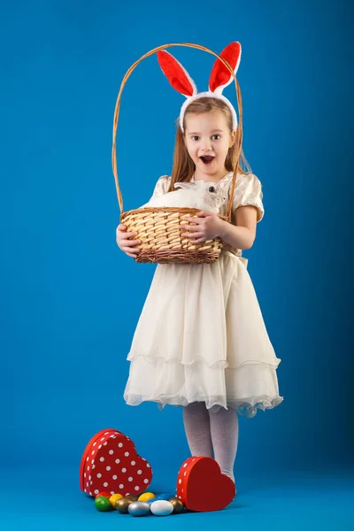 Nettes Mädchen mit weißem Kaninchen im Korb mit Ostereiern — Stockfoto
