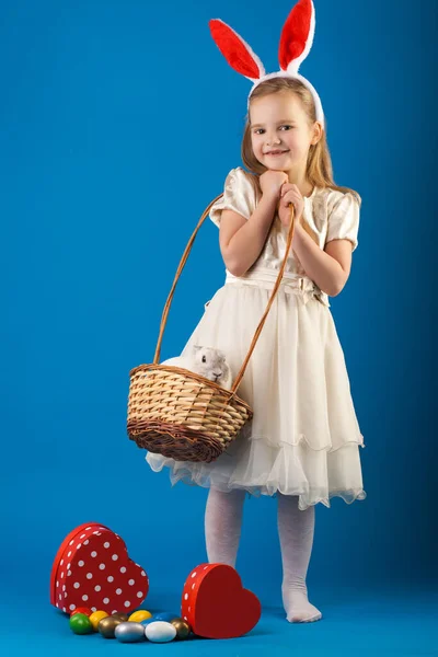 Симпатичная девушка с белым кроликом в корзине с пасхальными яйцами — стоковое фото