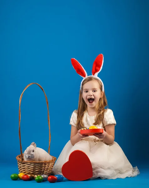 Nettes Mädchen mit weißem Kaninchen im Korb mit Ostereiern — Stockfoto