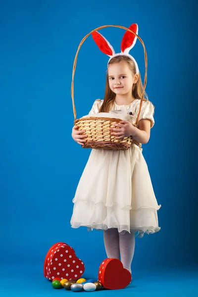 Nettes Mädchen mit weißem Kaninchen im Korb mit Ostereiern — Stockfoto