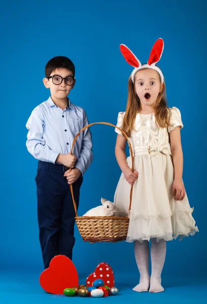 Netter Junge und Mädchen mit weißem Kaninchen im Korb mit Ostereiern — Stockfoto