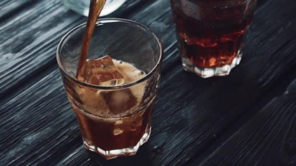 Cola wird in ein Glas mit Eis auf einem schwarzen Holztisch gegossen. — Stockvideo