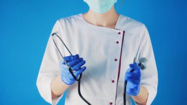 Elinde stentoskop olan beyaz önlüklü ve maskeli bir kadın doktor..