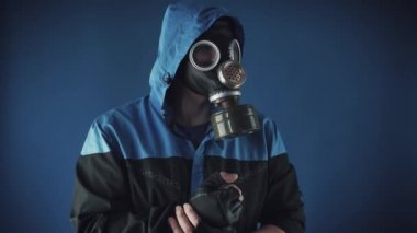 Mavi arka planda koruyucu başlıklı ve gaz maskeli bir adam.
