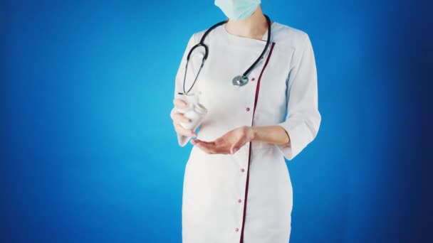 Medico donna in un cappotto bianco e maschera con una pillola in mano. — Video Stock