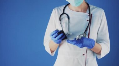 Beyaz önlüklü ve maskeli bir kadın doktor elinde bir hapla.