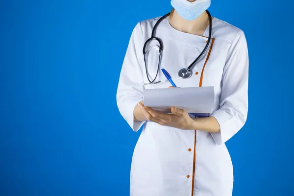 Female doctor in a white coat and mask with an recipe in her hands. — Stock Photo, Image