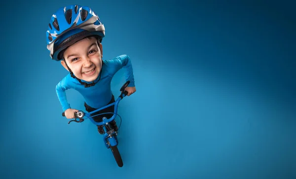 Kleine jongen met een fiets in een helm op een blauwe achtergrond. bovenaanzicht. — Stockfoto