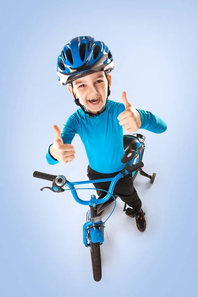 Kleine jongen met een fiets in een helm op een blauwe achtergrond. bovenaanzicht. — Stockfoto
