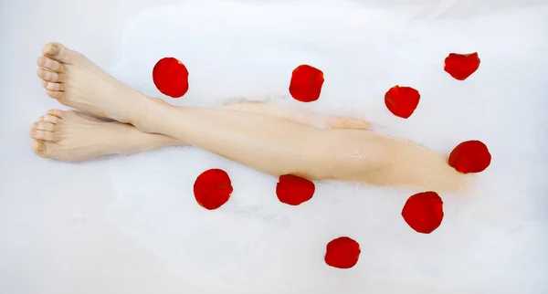 Legs of beautiful young female in bath with liquid soap and rose petals — Stock Photo, Image