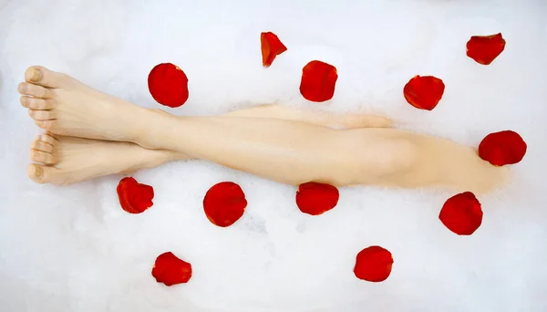 Hojas de guapa jovencita en bañera con jabón líquido y pétalos de rosa — Foto de Stock