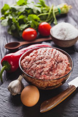 Sebze ve otlarla kaplı siyah bir arka planda çiğ et..