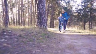 Annesiyle birlikte ormanda bisikletle gezen mutlu bir çocuk..