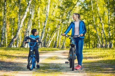 Mutlu bisikletçi çocuk güneşli ormanda annesiyle bisiklete biniyor.