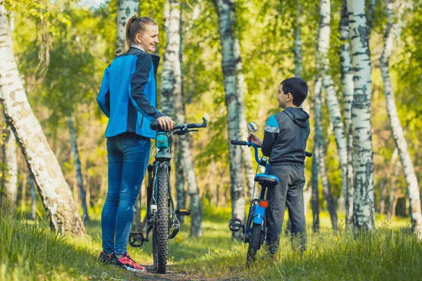 Happy kid cyclist rides a bike with mom in the sunny forest on a bike — Stock Photo, Image