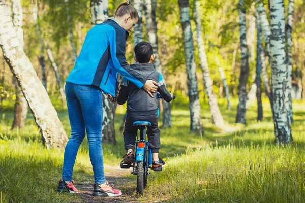 Lykkelig syklist som lærer å sykle med mamma i solskinnsskogen på sykkel – stockfoto