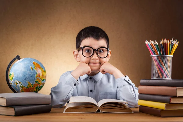Söt liten pojke skolpojke gör läxor vid ett bord med böcker — Stockfoto