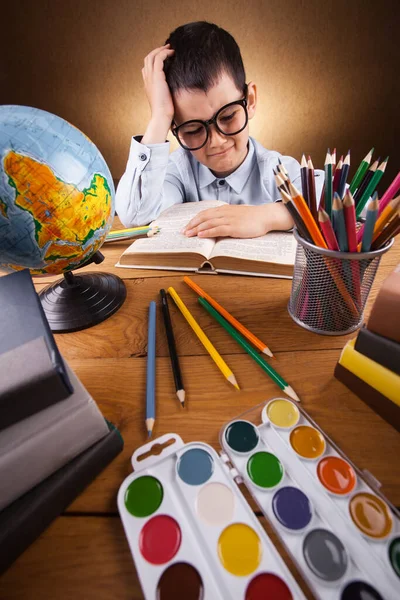 Söt liten pojke skolpojke gör läxor vid ett bord med böcker — Stockfoto