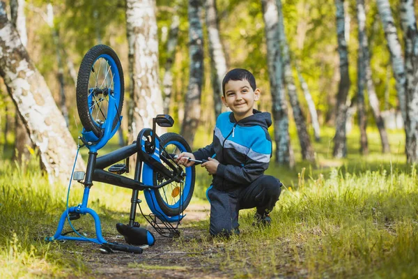 Pequeno ciclista rapaz balança uma roda quebrada em uma bicicleta. — Fotografia de Stock