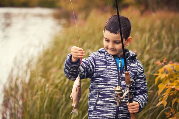Bonito menino pega peixe em um lago de verão. — Fotografia de Stock