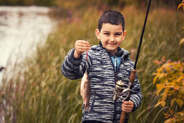 Bonito menino pega peixe em um lago de verão. — Fotografia de Stock