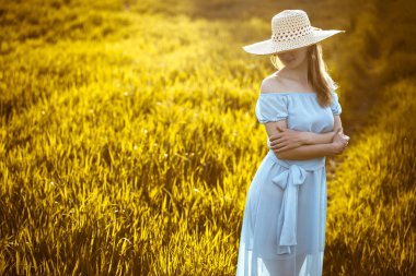 Buğday tarlasında duran genç bir kadın ve arka planda gün doğumu