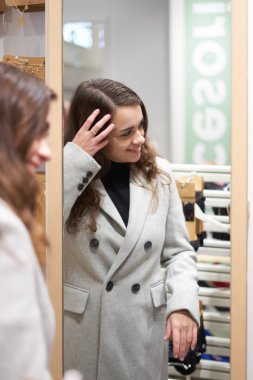 Genç bir kadın elbise mağazasında palto deniyor.