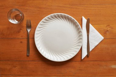 Ahşap arka planda porselen tabak ve çatal bıçak takımı.