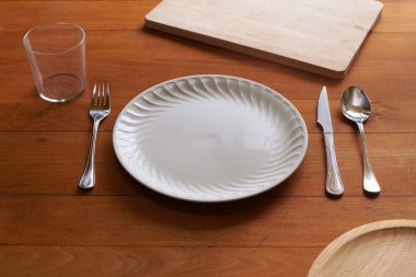 Ahşap arka planda porselen tabak ve çatal bıçak takımı.