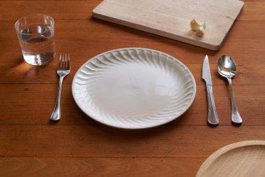 Akdeniz elementleriyle ahşap bir zemine karşı porselen tabak ve çatal bıçak takımı