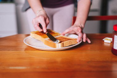 Tost üzerine tereyağı süren iki el.