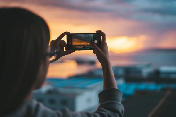 Kadın akıllı telefonuyla balkondan denizin fotoğraflarını çekiyor.