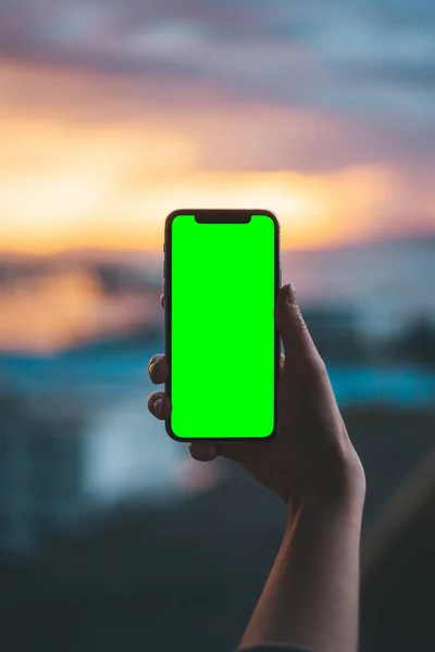 Hand holding a smartphone on a green screen