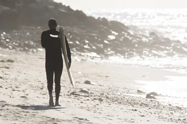 Male surfer walks the beach at sunrise