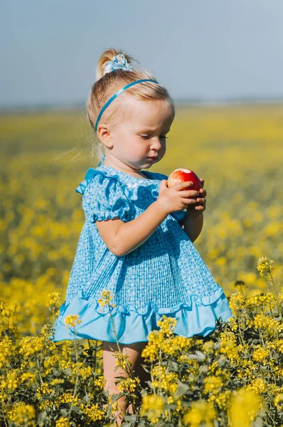 Menina com maçã no campo de flores amarelas — Fotografia de Stock