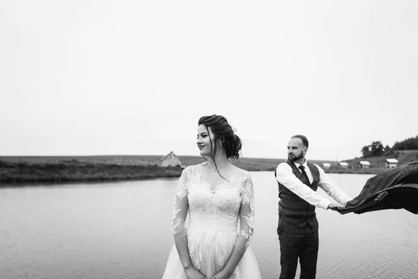 新婚夫婦は結婚式の日に湖の近く歩く — ストック写真