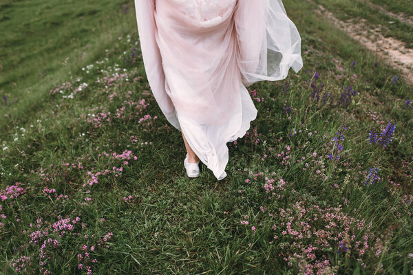Happy bride on wedding day. Go along the field flowers in the grass. Back view
