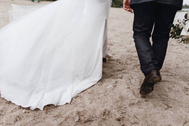 güzel düğün. yeni evliler kum yürüyor. Gelin lüks elbise ve güzel bir buket. Arkadan Görünüm. ayakları üzerinde kum Close-Up