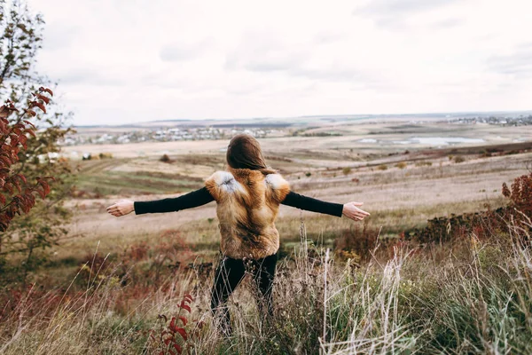 Rear view of woman wearing fur waistcoat putting hands on sides in freedom pose