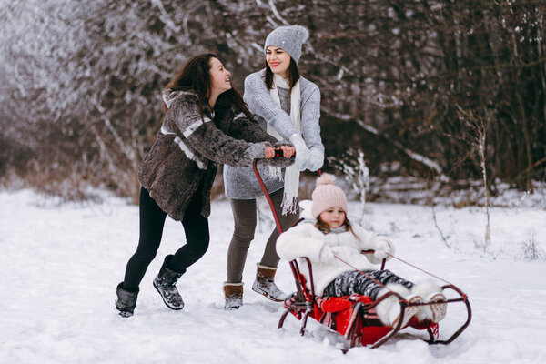 View of mother with elder daughter sledding smaller daughter and having fun on winter forest background