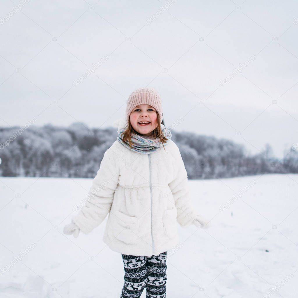 Front view of lttle girl standing and smiling in winter park
