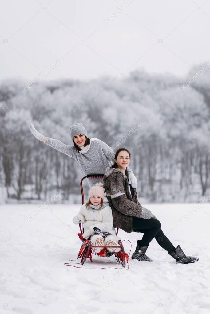 Mother with daughers walking in winter park and sledding smaller daughter
