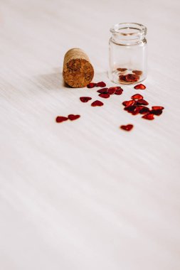 Açılan cam şişe ve bej renkli arka plan üzerinde kırmızı kalp şeklinde glitter kompozisyonu